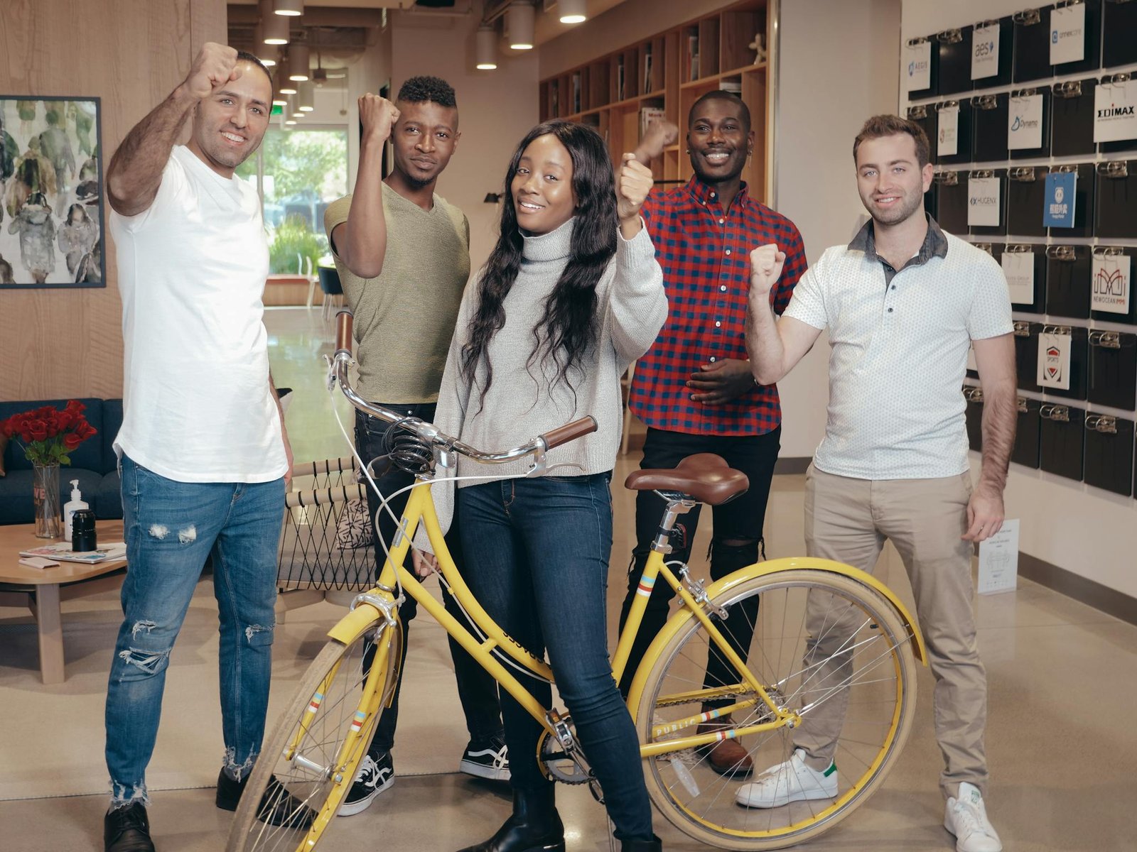 Diverse group of five adults standing indoors with a yellow bicycle, celebrating success.
